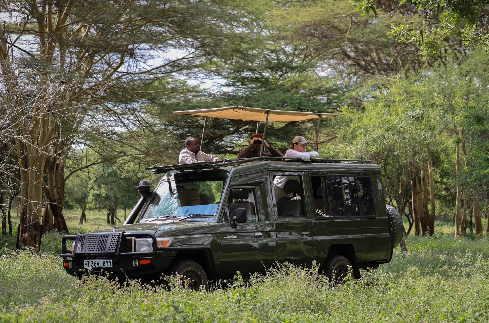 Safarové vozidlo se střešním oknem a toldou s turisty v africké krajině.