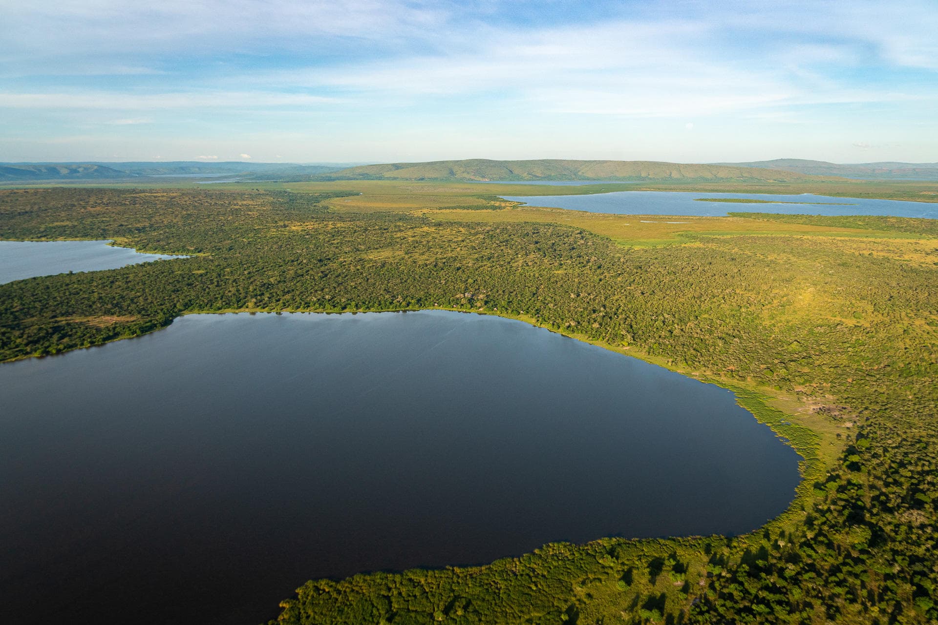 Letecký pohled na africké jezero obklopené lesem a travnatými pláněmi.